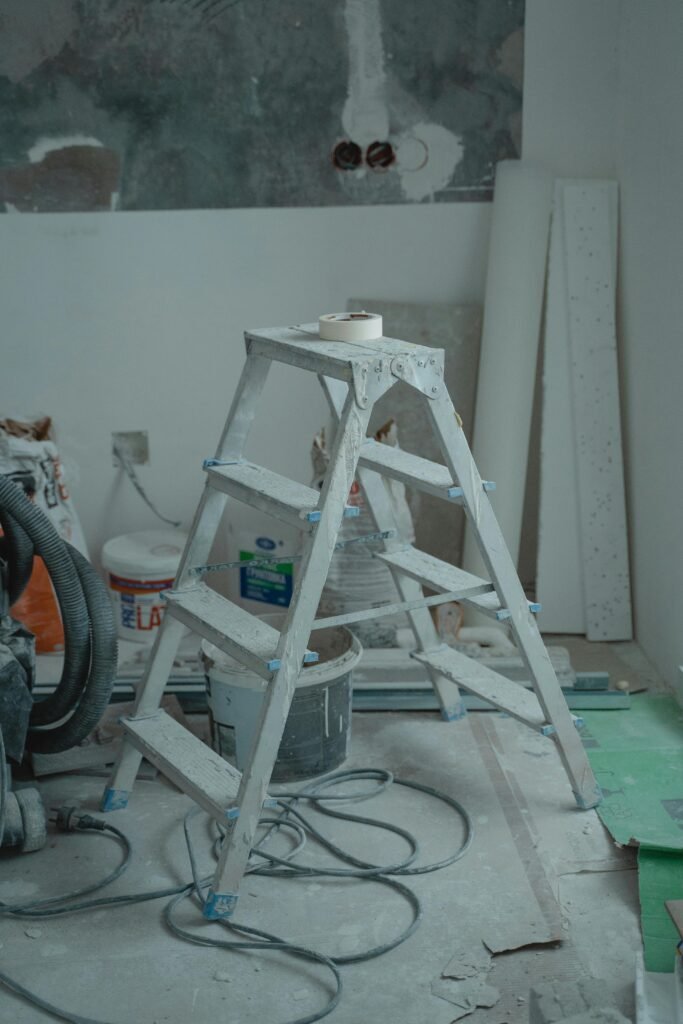 A metal ladder stands amidst renovation supplies including paints and plaster in an indoor setting.
